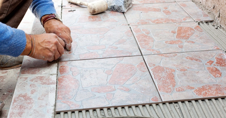 Person klebt Mosaikfliesen auf Betonboden in einem Baugebiet