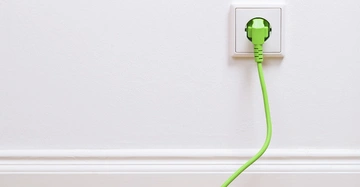 Ein grünes Kabel steckt in einer weißen Steckdose an einer glatten weißen Wand mit einer Fußleiste.
