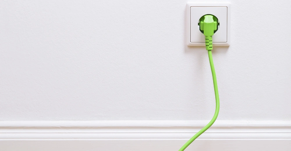 Ein grünes Kabel steckt in einer weißen Steckdose an einer glatten weißen Wand mit einer Fußleiste.