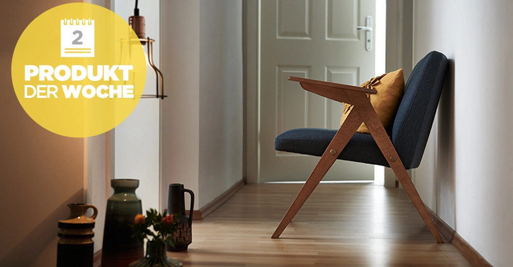 Ein blauer Stuhl mit gelbem Kissen steht in einem Flur vor einer geschlossenen Tür umgeben von Vasen und Pflanzen. Text Produkt der Woche 2