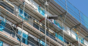 Gerüst mit Bauarbeiter arbeitet an Fassade eines Gebäudes blaue Plastikfolien bedecken einige Fenster klarer Himmel