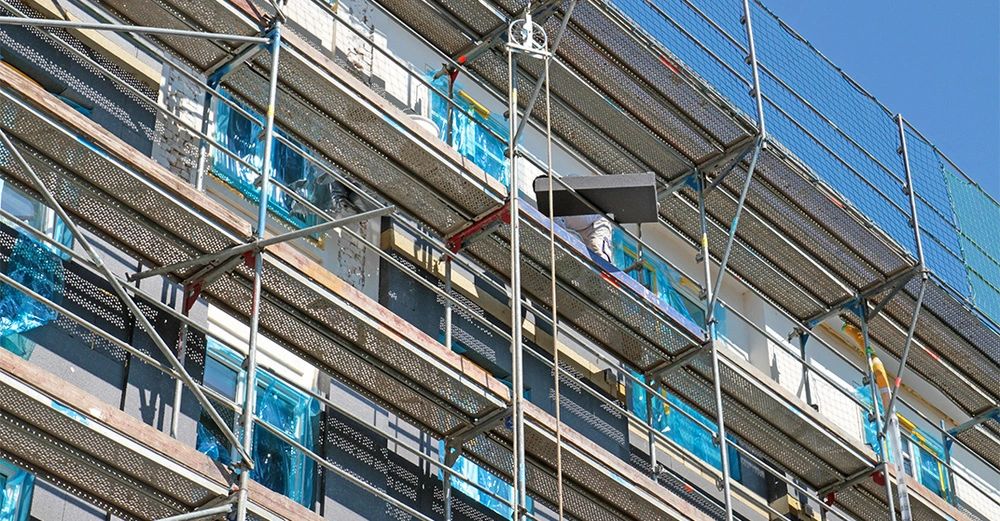 Gerüst mit Bauarbeiter arbeitet an Fassade eines Gebäudes blaue Plastikfolien bedecken einige Fenster klarer Himmel