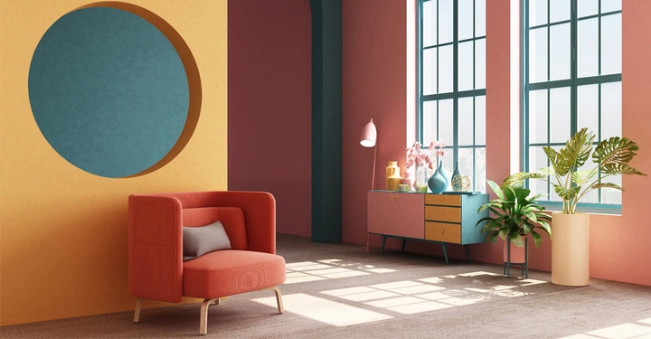 Colourblocking: senfgelbe Wand mit rundem, blauen Auslass, davor steht ein rostroter Ohrensessel. Im Hintergrund große Fenster und Topffplanzen am Boden. Sonne scheint durchs Fenster