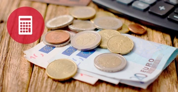 Münzen und Euro-Banknoten liegen auf einem Holztisch daneben eine Tastatur im Hintergrund links ein roter Kreis mit weißem Taschenrechner-Symbol.