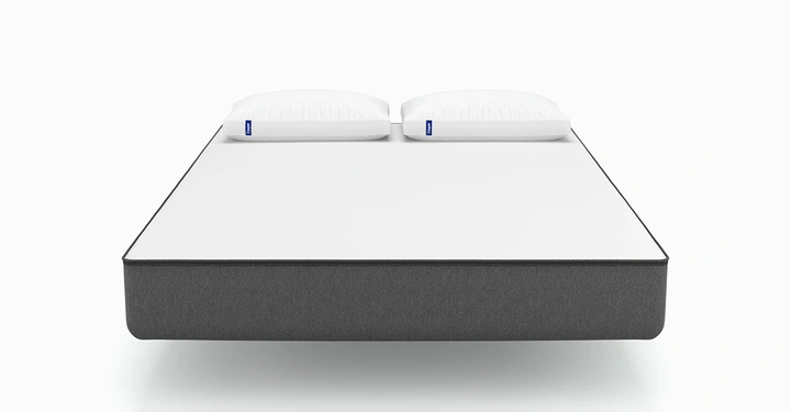 Galerie-Bild 3: Bett liegt still in minimalistischem metallrahmen Kontrast von schwarzem Rahmen und weißer Oberfläche Weiße Kissen beide mit blauem Logo auf einem ruhigen grund weißen Hintergrund.