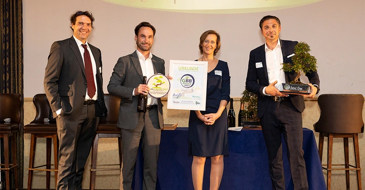 Galerie-Bild 7: Vier Personen präsentieren Auszeichnungen und Urkunden in einem Raum mit Stühlen und einem Tisch Hintergrund beinhaltet Pflanzen und Alkoholflaschen Urkunde mit Text: "URKUNDE GBB AWARD 2021" Firmenlogos unten