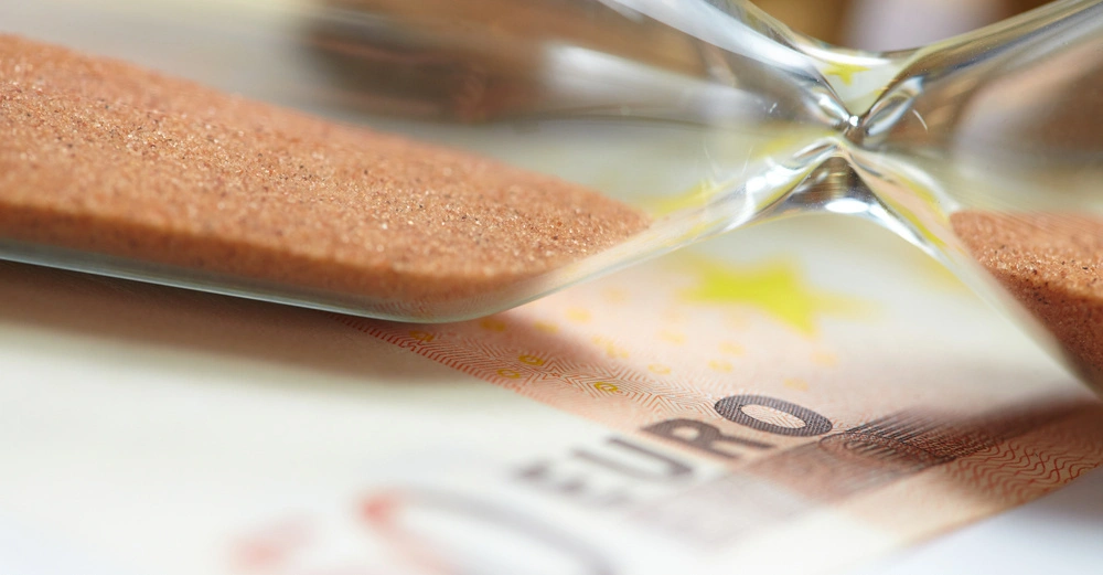 50-Euro Banknote auf der eine umgefallene Sanduhr mit orangem Sand liegt