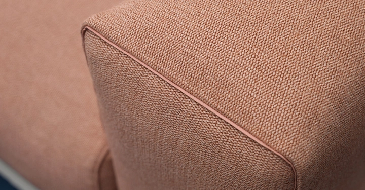 Eine Ecke eines rosa Sofas mit grob gewebtem Stoff in Nahaufnahme in einer hellen Umgebung.