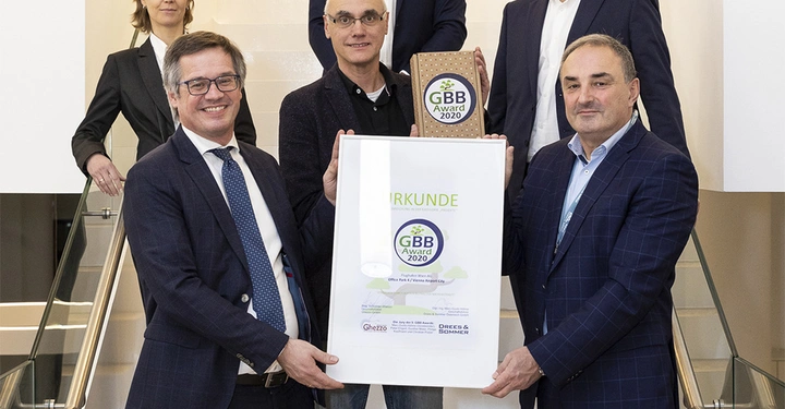 Eine Gruppe von sechs Personen steht auf einer Treppe in einem modernen Gebäude und hält eine Urkunde, auf der steht URKUNDE GBB Award 2020.