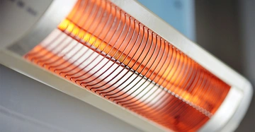 Rotglühender Heizstrahler hängt an der Wand in einem Innenraum und leuchtet orange.