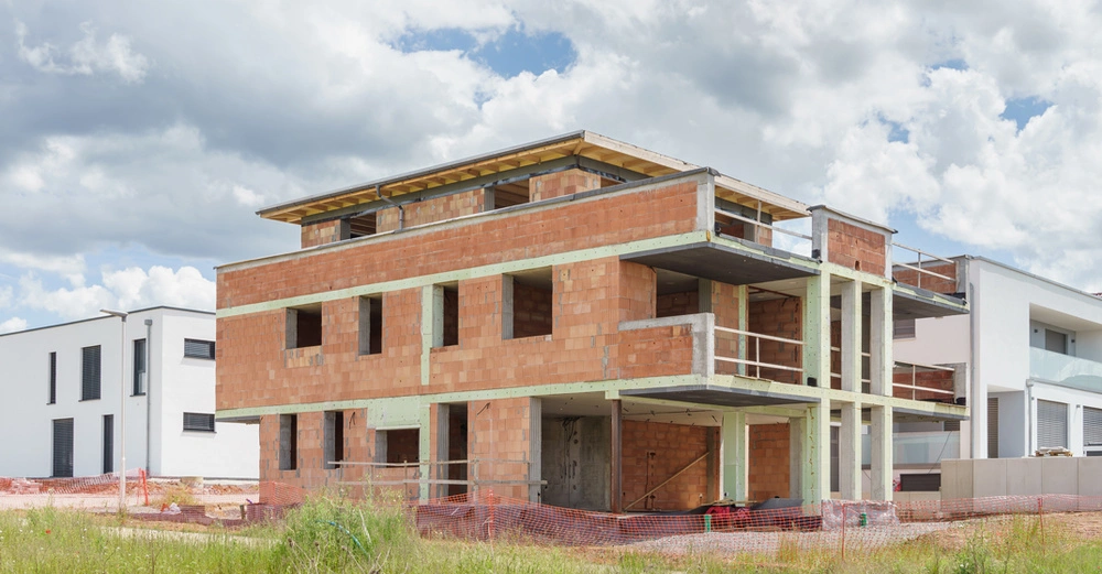 roter Ziegelrohbau mit Flachdach, dreistöckig steht in Neubausiedlung. Bewölkter Himmel.