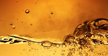 Blasen steigen in einer goldfarbenen Flüssigkeit auf dichter geschätzter Flüssigkeitshintergrund in einem warmen gelb-orangefarbenen Ton.