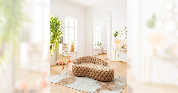 Galerie-Bild 4: Braunes Polstersofa steht auf gemustertem Teppich in elegantem Zimmer mit heller Wand weißem Fenster rundem Spiegel und Pflanzen. Zwei Flamingo-Statuen stehen neben dem Sofa.