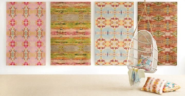 Vier bunte, gemusterte Teppiche hängen an einer Wand in einem hellen Raum vor einer beigen Bodenmatte links während ein weißer Hängesessel mit bunten Kissen rechts hängt.