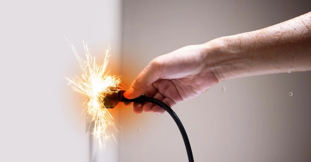 Hand hält ein defektes Stromkabel, aus dem Funken sprühen. Gefahr eines Stromschlags oder Kurzschlusses.