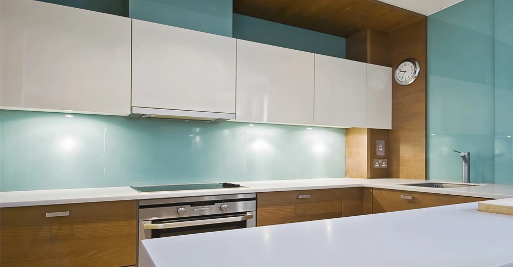 Moderne Küche mit Holz- und weißen Schränken Herd und Spüle in hell beleuchteter Umgebung Wanduhr und gläsernem Spritzschutzhintergrund.