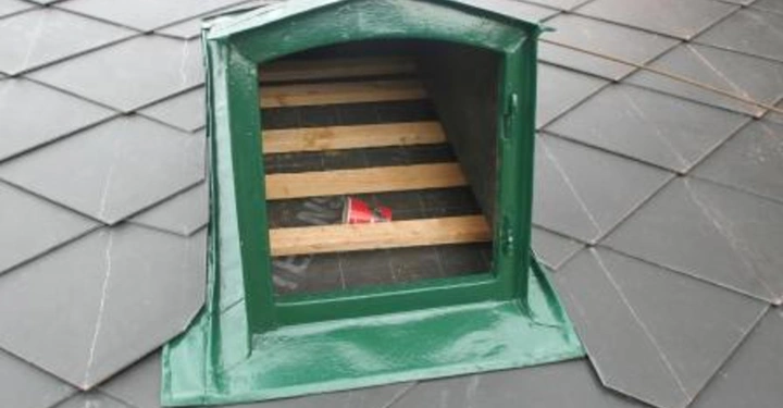 Galerie-Bild 12: Grünes belüftetes Fenster auf einem mit dunklen Ziegeln bedeckten Dach stehend Schlitze aus Holz im Inneren keine weiteren Objekte in der Umgebung