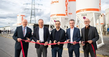 Fünf Männer halten ein rotes Band. Sie stehen nebeneinander und lächeln. Im Hintergrund stehen weiße Silos mit orangefarbenem "RÖFIX"-Logo auf einem Industriegelände.