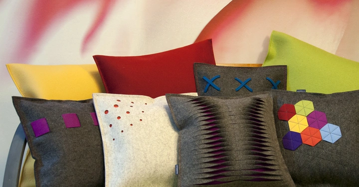 Galerie-Bild 2: Bunte Kissen liegen auf einem Sofa in einem Raum mit einer abstrakten bunten Wanddekoration im Hintergrund.