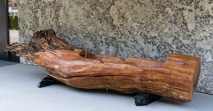 Holzbank liegt auf steinernen Blöcken vor einer grauen und schwarzen gemusterten Wand in einem Außenbereich
