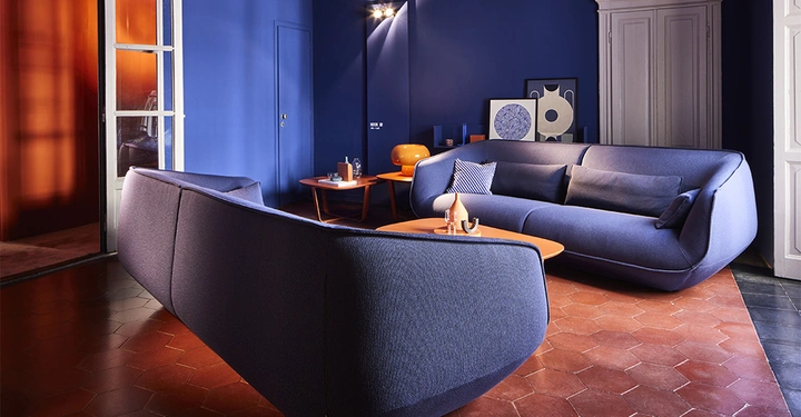 zwei Nook Sofas in Blaugrau stehen sich in blau gestrichenem Wohnzimmer gegenüber, kupferroter Fliesenboden und weiße Doppeltüre links im Bild.