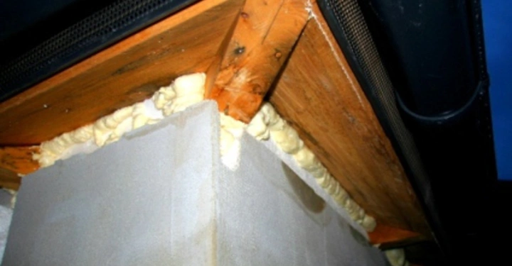 Galerie-Bild 10: Ein Betonblock ist mit Holzplatten abgedeckt und Dichtungsmasse füllt die Lücken. Das Ganze befindet sich an der Ecke eines Gebäudes unterhalb eines dunkelgrauen Dachs bei Abenddämmerung.