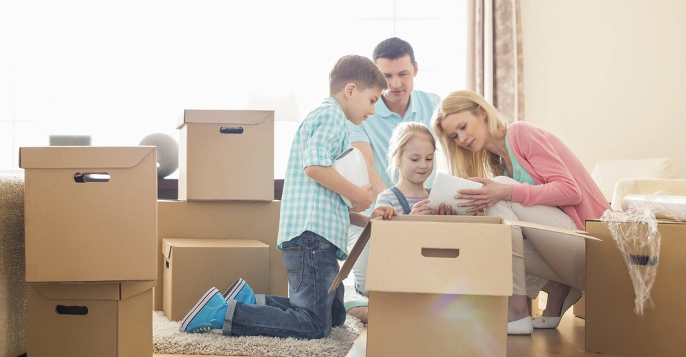Eine Familie packt gemeinsam Umzugskartons aus helle Wohnzimmerumgebung Möbel im Hintergrund Holzboden.