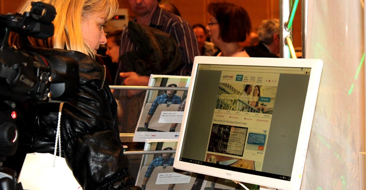 Galerie-Bild 10: Frau Betrachtet Monitor Messe Besucher im Hintergrund Text auf Monitor: Wohnnet Immobilien Bauen Themen Neubau Sanieren Einrichten Services Baufirmen Plaza Jobs News Dein extra Raum beim Bauen Giessen und Erliegen