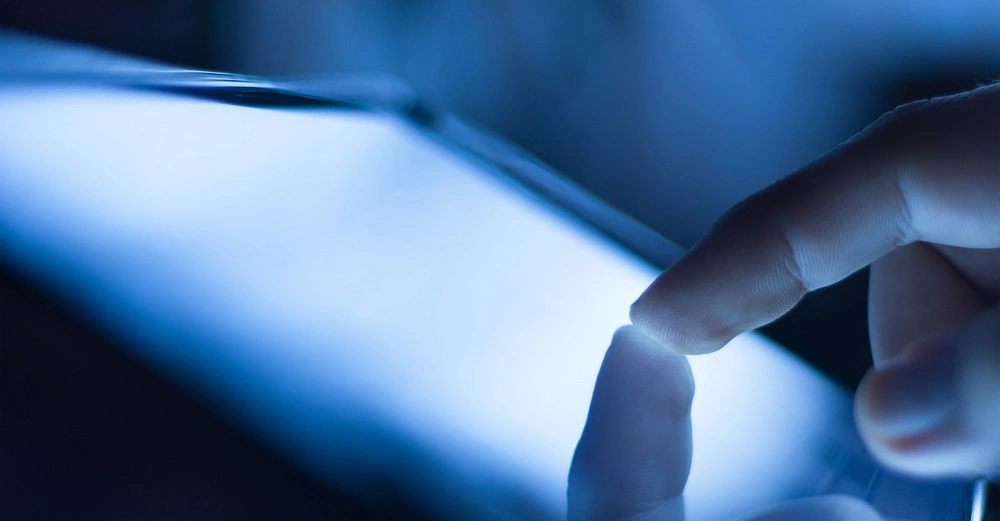 Finger tippt auf einen leuchtenden Touchscreen im dunklen Umfeld