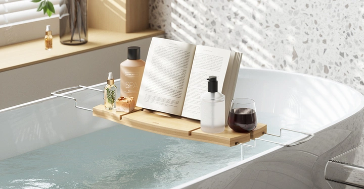 Badewanne mit Wasser gefüllt mit einem Badewannenregal aus hellem Holz auf dem ein aufgeschlagenes Buch liegt und eine Duftkerze steht. Rechts ein helles Fenster, Tageslicht.
