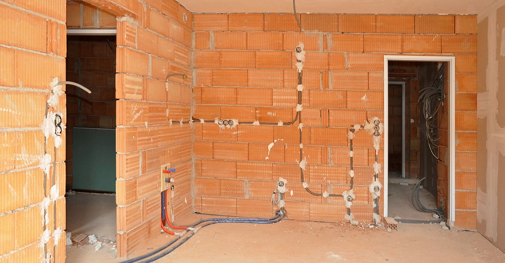 Rohbau aus rotem Ziegel, Innenraumansicht mit zwei Maueröffnungen für Innentüren in der gegenüberliegenden Wand und links im Bild