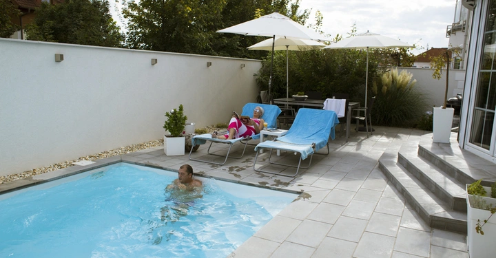Galerie-Bild 6: Mann schwimmt im Pool; Person auf Liegestuhl liest unter Sonnenschirmen; moderner Hinterhof mit Treppen und Pflanzen.
