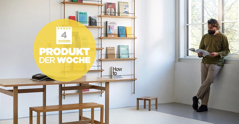 Zeitschriftenregal Magazine Shelving von dänischem Designhaus Moebe in hellem Raum. Links am Fenster junger Mann der liest.