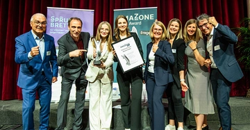 Bühnen-Gruppenbild der fröhlichen Gewinnerinnen im Kreis weiterer Baumit-Mitarbeiter wie Geschäftsführer und Ausbildungsleiter. Preisträgerinnen halten Urkunden in der Hand.
