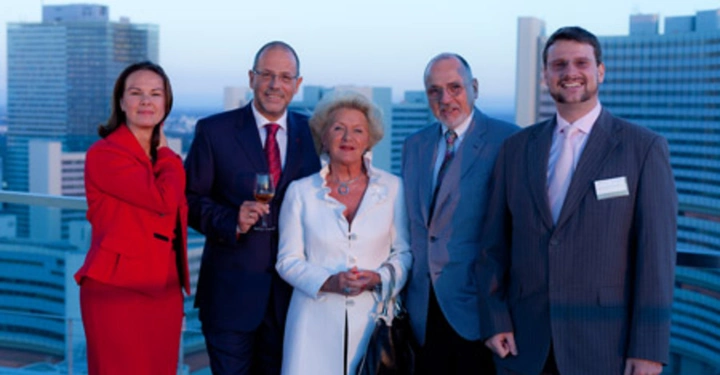 Galerie-Bild 24: Fünf Menschen stehen lächelnd zusammen auf einer Dachterrasse vor einer Aussicht auf moderne städtische Hochhäuser im Hintergrund eine Frau und vier Männer zwei in Anzügen und einer in einem weißen Mantel