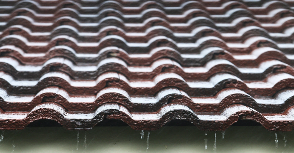 Braune gewellte Dachziegel mit laufendem Regenwasser in einer nahen Ansicht dachen in einer regnerischen Umgebung