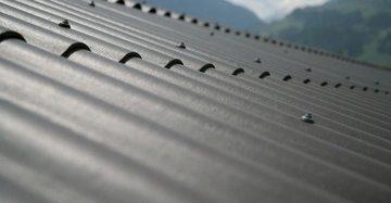 Wellblechdachstruktur mit Schrauben in Nahaufnahme ruhig in Berglandschaft bei bewölktem Himmel Hintergrund.