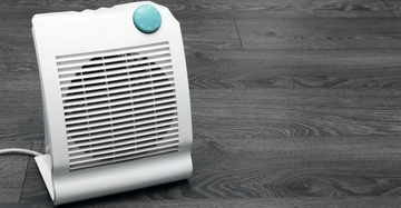 Ein weißer elektrischer Heizlüfter mit einem blauen Drehknopf steht auf einem dunklen Holzfußboden.