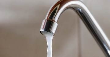 glänzender Chromwasserhahn, Wasser rinnt in dünnem Rinnsal aus dem Hahn, Hintergrund nicht erkennbar