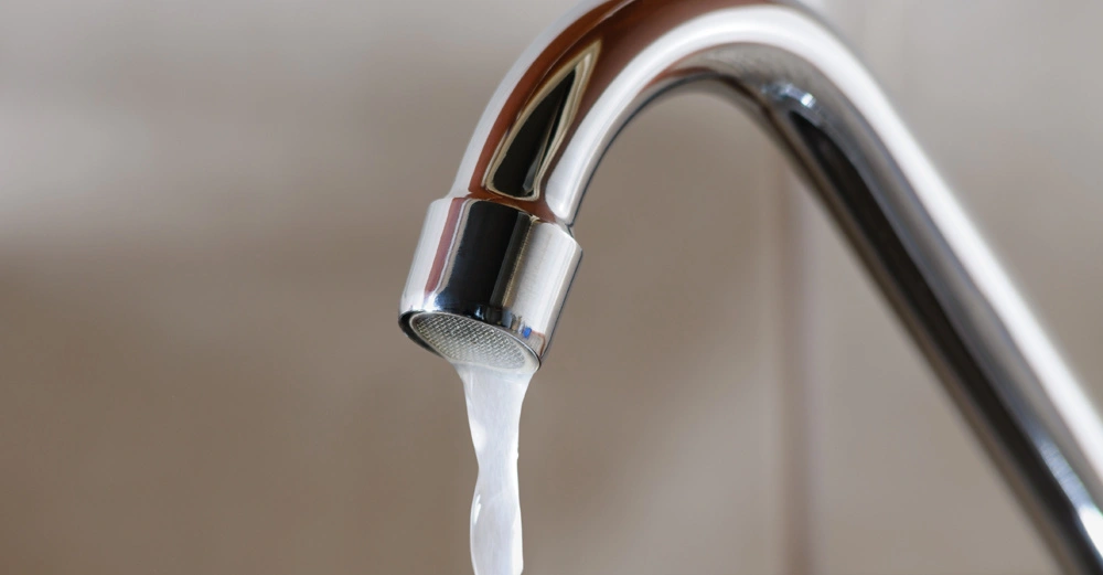 glänzender Chromwasserhahn, Wasser rinnt in dünnem Rinnsal aus dem Hahn, Hintergrund nicht erkennbar