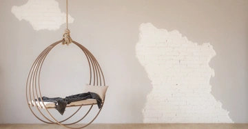 Kreisschaukel hängt an einem Seil mit Kissen und Decke darauf an einer grob weiß gestrichenen Ziegelwand in einem hellen minimalistischen Raum