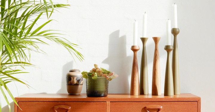 Möbel sind eine Holzkommode auf der drei Kerzenhalter mit brennenden Kerzen und zwei Vasen stehen neben einer grünen Topfpflanze im Raum.