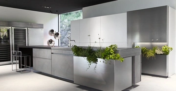 Hochmoderne Küche mit Insel aus Edelstahl und Beton, dekoriert mit Pflanzen. Die Küche hat Edelstahlgeräte, hängende Kugellampen, Fenster mit Blick auf Felsen und zwei Barhocker.