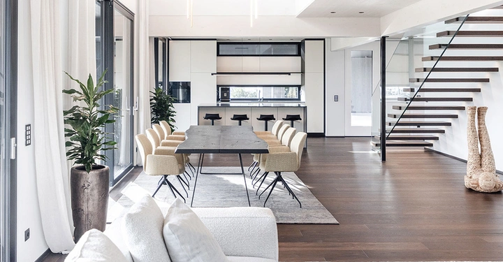 Innenaufnahme des Floating House, weiße Couchlandschaft im Vordergrund, rechts eine dunkle, freischwebende Treppe, die ins Obergeschoß führt.