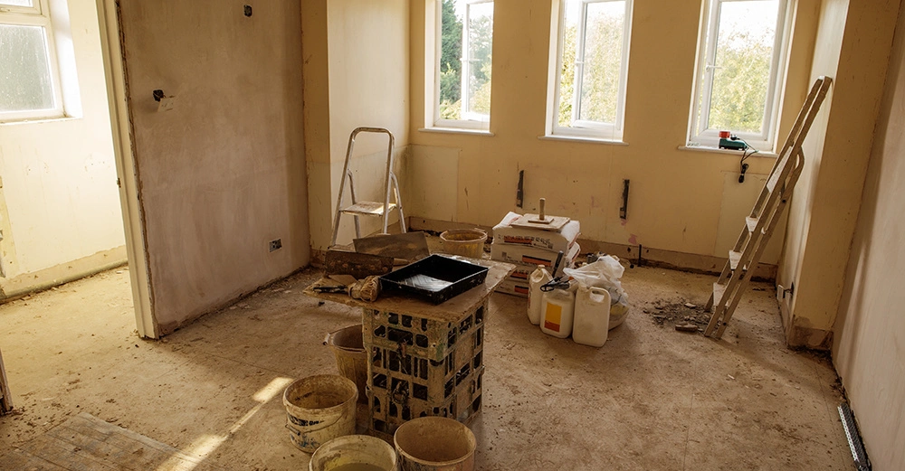 Eine fast fertige Baustelle Eimer Farbwannen und Gipskartonplatten auf dem Boden Putzleitern im Raum und Tageslicht durch drei Fenster im Hintergrund hellt den Raum auf