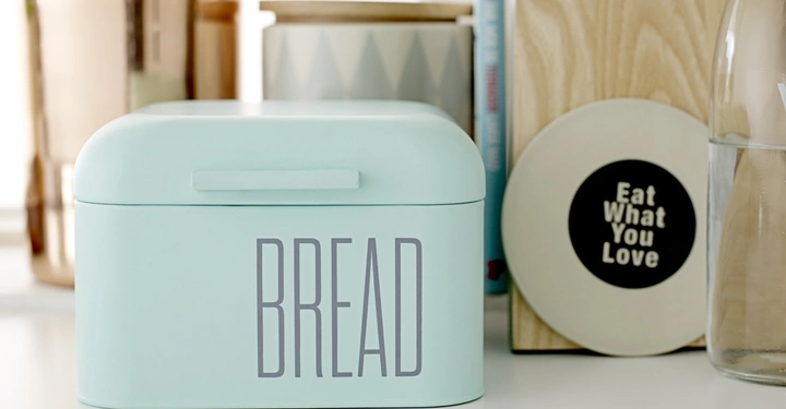 Galerie-Bild 5: Mintgrüne Brotdose steht auf einer Küchenarbeitsplatte zwischen anderen Küchenutensilien. Auf der Dose steht das Wort BREAD. Im Hintergrund befindet sich ein rundes Schild mit dem Text Eat What You Love.