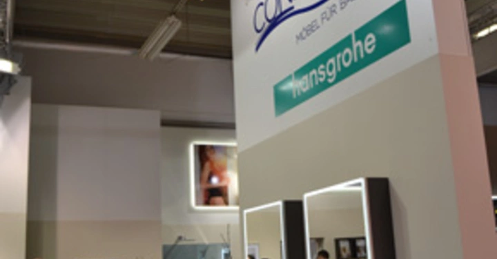 Galerie-Bild 6: Person schaut in eine geöffnete Schublade vor einem Waschtisch mit Spiegeln und Waschbecken in einer Badshowroom-Umgebung Text Artweger CONFORM Möbel für Bäder hansgrohe ist auf einem großen Schild darüber zu sehen