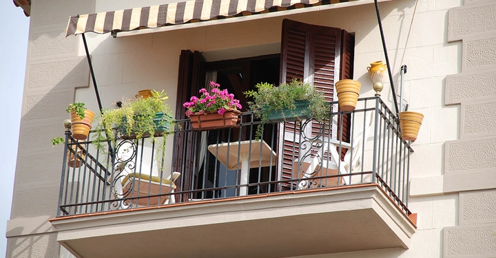 Die Planung eines mediterranen Balkons mit schmiedeeisernem Geländer, einer Markise als Sonnenschutz und üppiger Bepflanzung in Blumenkästen.