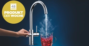 Eine Hand bedient einen glänzenden Wasserhahn, der heißes Wasser in eine Tasse mit roter Flüssigkeit gießt vor einem dunklen Hintergrund. Text: 48 PRODUKT DER WOCHE.