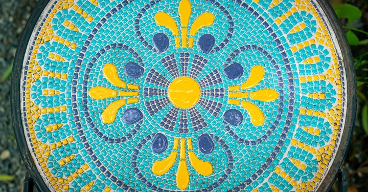 Galerie-Bild 1: Mit türkisen, blauen und gelben Mosaiksteinchen verzierte Tischplatte eines runden Gartentischs
